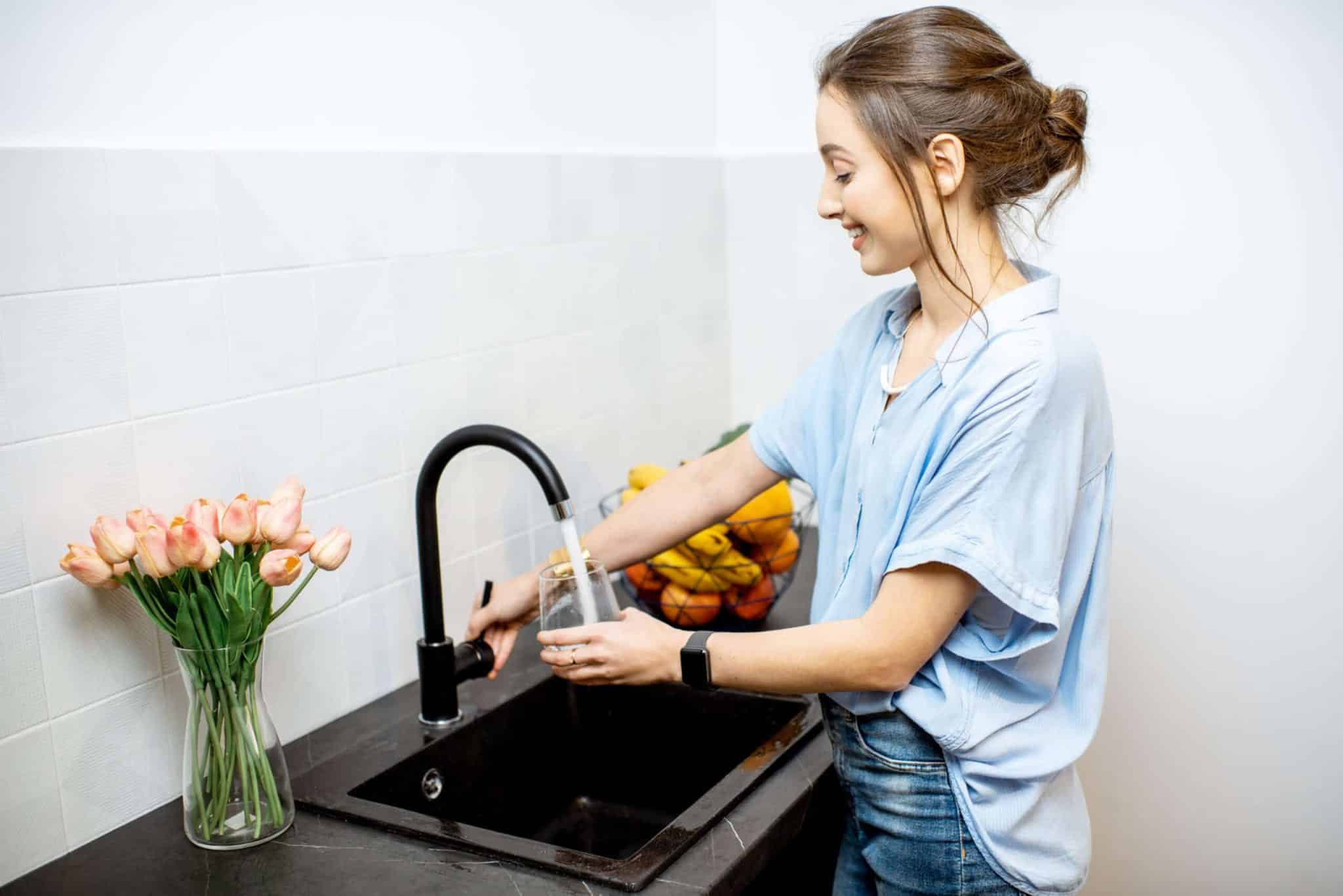 Woman filling glass with tap water for drinking on the kitchen